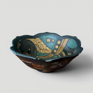 May include: A decorative bowl with a dark green, gold, and teal interior. The bowl has a unique, scalloped edge and a geometric design. The exterior is a dark brown with a patchwork design. A unique piece for home decor.