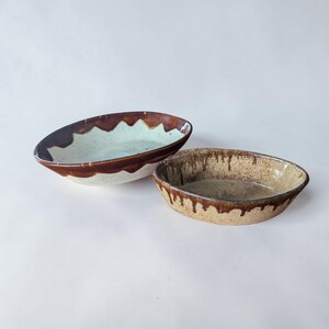Peut inclure: Deux bols ovales en céramique. Le plus grand a un intérieur bleu clair avec un bord marron et un extérieur blanc. Le plus petit a un intérieur beige moucheté et un bord marron dégoulinant.