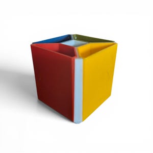 May include: A multi-coloured desk organiser with four compartments. The organiser is a cube shape with red, yellow, blue, and green sides. A white strip runs vertically along one edge. The interior compartments are white.