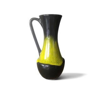 Peut inclure: Pichet en céramique avec une anse. Le haut et le bas sont noirs, tandis que la section centrale est jaune vif. Le pichet a une finition brillante et une anse incurvée, idéal pour servir des boissons ou comme objet décoratif.