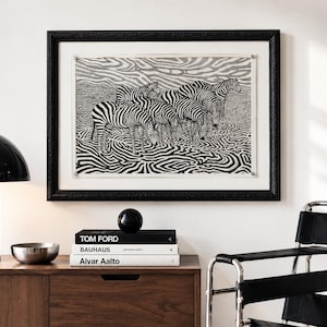 Peut inclure: Une impression d'art encadrée en noir et blanc représentant un troupeau de zèbres dans un paysage aux motifs rayés ondulants. L'œuvre est placée dans un cadre noir texturé avec un passe-partout blanc, au-dessus d'un meuble en bois.