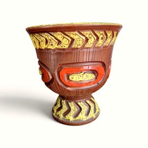 May include: A brown ceramic chalice featuring a wide rim and a pedestal base. The exterior is decorated with textured yellow chevron patterns around the top and bottom, and prominent orange oval accents with yellow centres on the body.