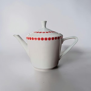 May include: White ceramic teapot with a lid, featuring a red polka dot pattern around the rim and lid. The teapot has a curved spout and a handle. The design is simple and elegant, suitable for serving tea.