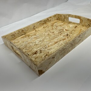 May include: A rectangular serving tray with a light wood grain pattern. The tray has a natural, light brown colour with darker brown and tan accents. It features cut-out handles on the short sides for easy carrying. Suitable for serving food or displaying items.