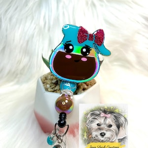 May include: A teal coffee pot badge reel with a pink glitter bow, brown coffee, and a cute face. The badge reel has iridescent trim and a beaded accent. A small illustration of a dog is in the corner.