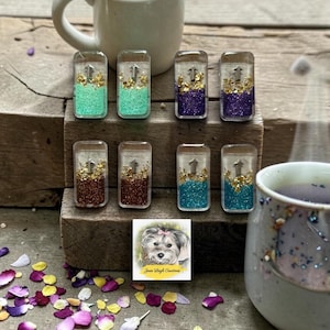May include: Eight rectangular resin dominoes featuring a clear top section, a central silver arrow, and a bottom section filled with colored glitter and gold leaf flakes. The colors include mint green, purple, brown, and teal, arranged in two rows.