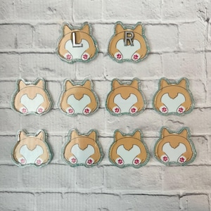 May include: Ten acrylic charms shaped like the rear view of a corgi dog, featuring tan and white fur patterns with pink paw pads. Two charms are marked with the letters L and R in silver, while the remaining eight charms are plain.
