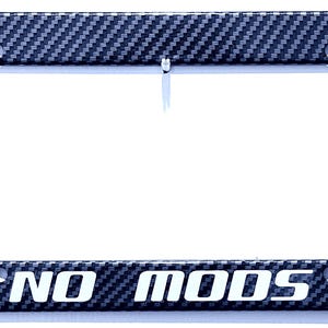 May include: A rectangular license plate frame featuring a black and grey carbon fiber pattern. The bottom horizontal bar displays the text NO MODS in bold, white, capital letters. The frame includes four mounting holes for vehicle attachment.