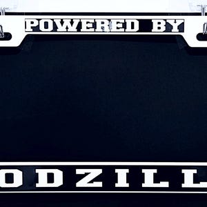 Powered By Godzilla White Metal License Plate Frame