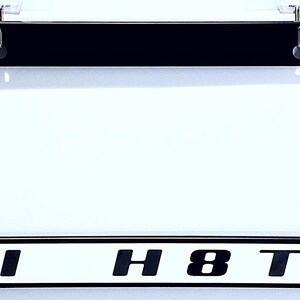 May include: Black license plate frame with a clear cover. The bottom of the frame has the text "HI H8TR" in bold, black letters on a white background. The frame is rectangular and has a black border.