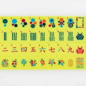 May include: A set of yellow Mahjong tiles with various symbols, numbers, and Chinese characters. The tiles feature colorful dots, bamboo stalks, and floral designs. Some tiles have the word "JOKER" printed on them.