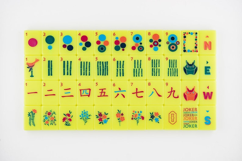 May include: A set of yellow Mahjong tiles with various symbols, numbers, and Chinese characters. The tiles feature colorful dots, bamboo stalks, and floral designs. Some tiles have the word "JOKER" printed on them.