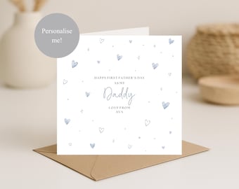 May include: A white greeting card with blue watercolor hearts and the text "Happy First Father's Day as my Daddy Love from Ava." The card is on a brown envelope. A gray circle with the text "Personalise me!" is in the upper left corner.