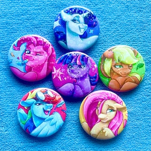 May include: A collection of six round buttons featuring colorful illustrations of cartoon ponies. Each button showcases a different pony with unique designs and vibrant color schemes, set against a blue background.