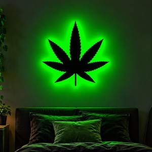 Op de afbeelding: Een wandgemonteerd LED-bord met een effen zwart cannabisblad-silhouet gecentreerd tegen een levendige, gloeiende groene lichtkrans die de omgeving verlicht met een helder, neonachtig effect.