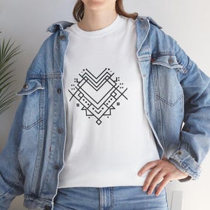 May include: White t-shirt with a black geometric heart design. The heart is made up of lines, dots, and geometric shapes. The shirt is worn with a denim jacket and blue jeans.