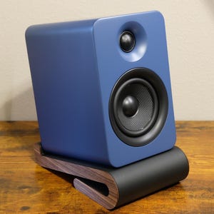 Peut inclure: Un haut-parleur bleu avec un cône de haut-parleur noir et un petit haut-parleur noir au-dessus. Le haut-parleur est sur un support en bois avec une base noire. Le support est sur une surface en bois.