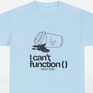 Puede incluir: Camiseta azul claro con un gráfico negro de una taza de café derramada y el texto "I can't function() RIGHT NOW". El diseño presenta una taza de café de dibujos animados con una cara triste.