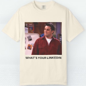 Puede incluir: Camiseta de color crema con una imagen serigrafiada de un hombre con una camisa roja y el texto "WHAT'S YOUR LINKEDIN". La imagen es de un programa de televisión.