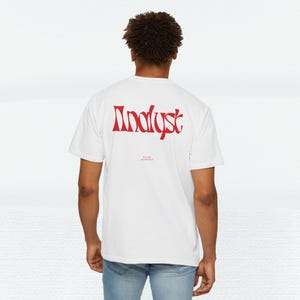 May include: White t-shirt with the word "Analyst" in red, stylized font across the back. Below the word is smaller text. The shirt is worn by a person in blue jeans.