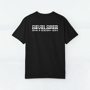 May include: Black t-shirt with the word "DEVELOPER" printed in white, stacked three times. The shirt has short sleeves and a crew neck. The text is centered on the back of the shirt.