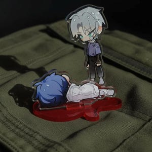 May include: Two anime-style acrylic figures. One figure is standing, with gray hair, a purple jacket, and black pants. The other figure is lying down with blue hair and a white outfit, on a red guitar-shaped base. The background is a green fabric.