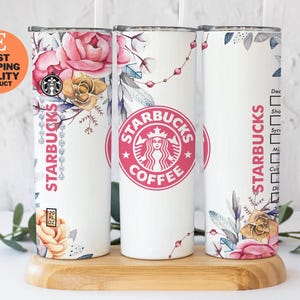 May include: Three white Starbucks tumblers with floral designs and the Starbucks logo. The tumblers feature pink roses, gold accents, and the Starbucks logo in pink. Each tumbler is 20 fl oz.