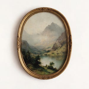 May include: An oval framed landscape painting. The artwork shows a tranquil mountain lake scene with green hills and a misty sky. The frame is ornate, with a gold finish. The painting is a classic piece of art.