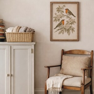 May include: A framed print depicting two robins on a flowering branch, set in a room with a chair and cabinet. The artwork has a vintage style with a wooden frame. The room also features a basket of folded textiles, creating a warm, inviting atmosphere.