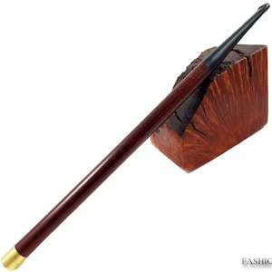 May include: A long, dark brown smoking pipe with a black mouthpiece and a gold-colored metal end. The pipe rests on a textured, reddish-brown wooden block. The words "FASHION PIPES" are printed in the bottom right corner.