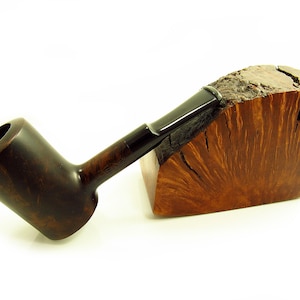 Könnte beinhalten: Eine dunkelbraune Holzpfeife mit einem schwarzen Mundstück, die auf einem Holzblock mit einzigartiger Maserung liegt.