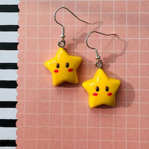 May include: A trio of cream-glazed ceramic mugs with a speckled finish. Each mug is adorned with a hand-painted design: a blue and green leaf, a yellow flower, and a red berry. The mugs have a simple, modern design.