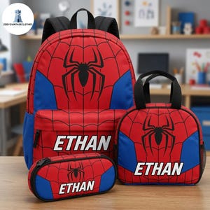May include: A red and blue backpack, lunch bag, and pencil case set featuring a black spider web pattern and a large black spider emblem. Each item is personalized with the name ETHAN in white capital letters on the front pocket area.