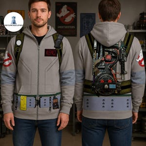 May include: A light gray zip-up hoodie featuring a printed Ghostbusters proton pack on the back and a utility belt design on the front. The sleeves display the Ghostbusters logo, and a black name patch with the text KLEPACZ is on the chest.