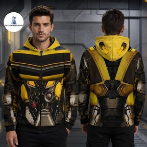 May include: A yellow and black zip-up hoodie featuring a detailed mechanical robot-inspired print on the front and back. The design includes metallic textures, dark grey paneling, and a hood with yellow accents, mimicking a robotic exoskeleton.