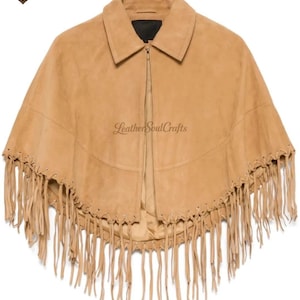 May include: A tan suede cape featuring a pointed collar, a central zipper closure, and long fringe detailing along the bottom hem. The garment includes a horizontal seam across the chest and is branded with the text Leather Soul Crafts.