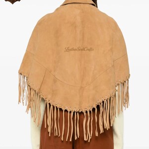 May include: A tan suede cape featuring a collared neckline and a curved hemline adorned with long, thin fringe detailing. The garment includes decorative lacing along the lower edge and displays the text LeatherSoulCrafts in the center.