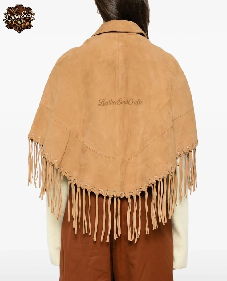 May include: A tan suede cape featuring a collared neckline and a curved hemline adorned with long, thin fringe detailing. The garment includes decorative lacing along the lower edge and displays the text LeatherSoulCrafts in the center.