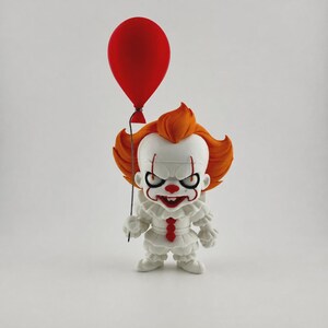 Pu&ograve; includere: Una statuina bianca di un clown con capelli arancioni e un palloncino rosso. Il clown ha un'espressione sinistra, naso e bocca rossi e un colletto a balze. Il palloncino &egrave; attaccato a un filo sottile.