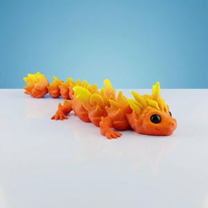 May include: A multi-segmented articulated dragon figurine featuring a vibrant gradient of orange and yellow colors. The creature has a smooth, matte texture, prominent spikes along its back, and large, round, solid black eyes on its head.
