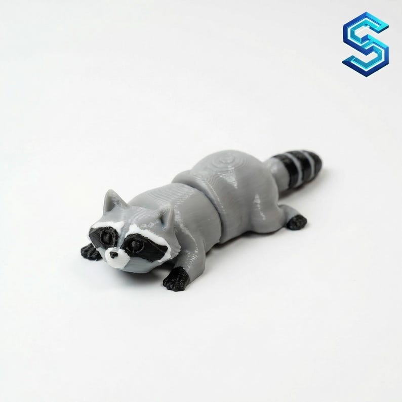 May include: A small, articulated 3D printed raccoon figurine in shades of grey, black, and white. The raccoon features a characteristic black eye mask, pointed ears, and a striped tail, with a smooth, layered texture typical of additive manufacturing.