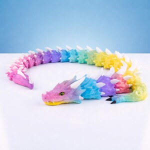 May include: A multi-colored articulated dragon figurine featuring a gradient of pink, purple, blue, green, and yellow segments. The dragon has white spikes along its back, a detailed head with yellow eyes, and black-tipped claws on its tail end.
