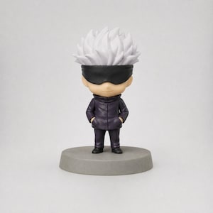 Pu&ograve; includere: Piccola statuetta di un personaggio con capelli bianchi a spillo, una benda nera e un cappotto viola scuro. La figura &egrave; in piedi su una base circolare grigia. Lo sfondo &egrave; bianco.
