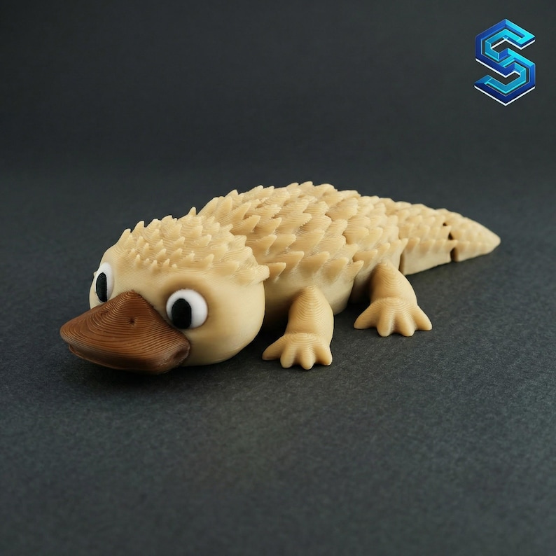 May include: A 3D printed articulated platypus figurine in a light beige colour with a dark brown bill and black and white eyes. The creature features a textured, spiky back and a segmented body design that allows for movement and flexibility.