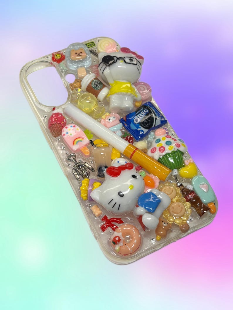 Pu&ograve; includere: Custodia trasparente per telefono decorata con vari ciondoli colorati, tra cui un personaggio di Hello Kitty, una sigaretta, un biscotto Oreo, un cupcake e una tazza di caff&egrave;. La custodia ha una variet&agrave; di altri piccoli oggetti decorativi.