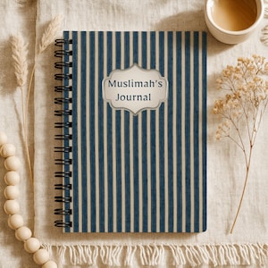 Pode incluir: Um diário com espiral com uma capa listrada azul e creme. A capa apresenta o texto "Muslimah's Journal" em um rótulo decorativo. O diário está aberto, revelando a encadernação em espiral e as páginas em branco. O diário está em uma superfície creme.