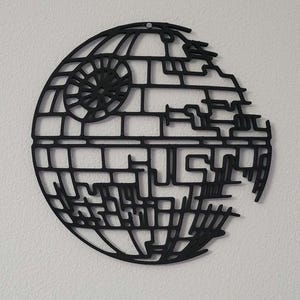May include: A black, circular wall decoration featuring a detailed, open-frame lattice design that mimics the appearance of a spherical space station. The structure includes a prominent circular dish detail on the upper left side and geometric lines.