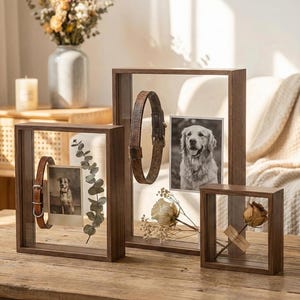 Könnte beinhalten: Eine Sammlung von Holz-Schattenbox-Rahmen in verschiedenen Größen. Jeder Rahmen enthält ein anderes Objekt, darunter ein Hundehalsband, ein Schwarz-Weiß-Foto eines Hundes und Trockenblumen. Die Rahmen werden auf einer Holzoberfläche präsentiert.