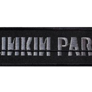 Könnte beinhalten: Ein rechteckiger, schwarz bestickter Aufnäher mit dem Text LINKIN PARK in grauem Garn. Die Schrift ist stilisiert mit einer horizontalen Linie durch die Mitte und kleinen klammerartigen Symbolen an den linken und rechten Rändern.