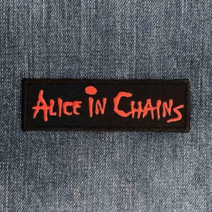 May include: A rectangular black embroidered patch featuring the text Alice in Chains stitched in a bright red, stylised font. The patch has a clean, finished border and is designed for application onto fabric surfaces like denim or other textiles.